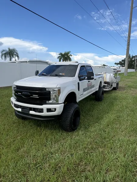 White lifted pickup with Patrick's Pressure Washing door lettering towing a trailer with water tanks, parked on grass