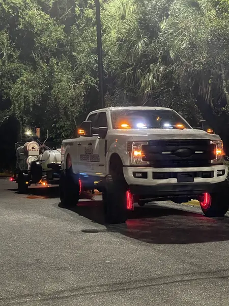Night view of a pickup with amber roof lights and red wheel lights towing a trailer with hose reels and tanks