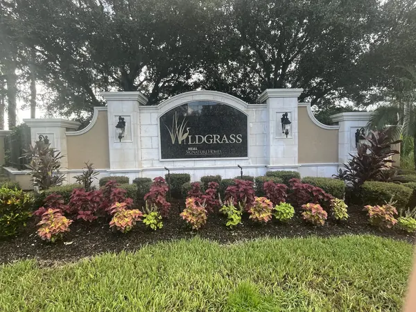 Stone entrance sign for a residential community with flowering landscaping in front under an overcast sky