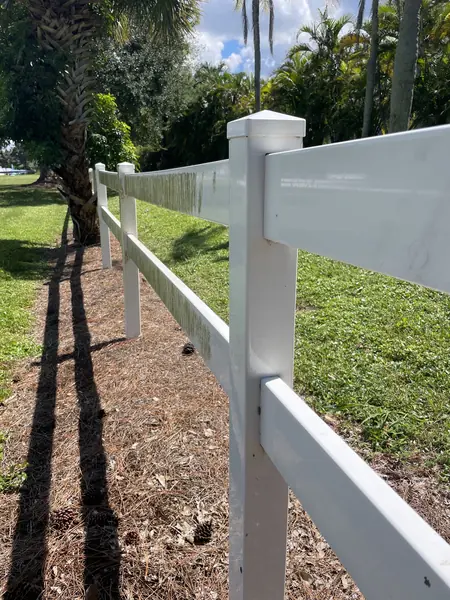 Clean white vinyl fence running beside a mulch bed and lawn in sunlight