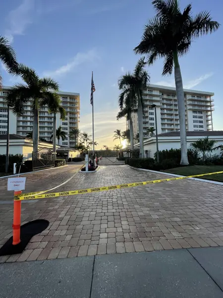 Brick paver entrance drive to a gated condo tower complex with caution tape and a flag at sunset