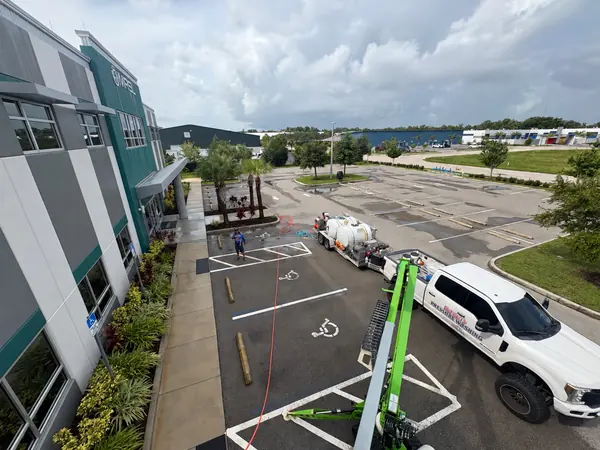 High view of a commercial office entrance and lot with a white pressure washing truck, trailer, green lift and a worker