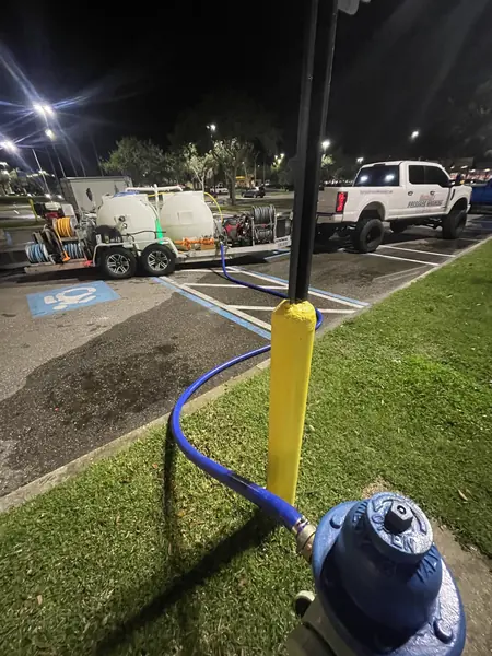 Blue hose connected to a fire hydrant beside a yellow bollard, with the pressure washing rig parked in a lot at night