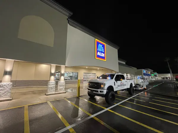 Pressure washing truck and trailer parked on a wet lot in front of a supermarket entrance at night with yellow lines