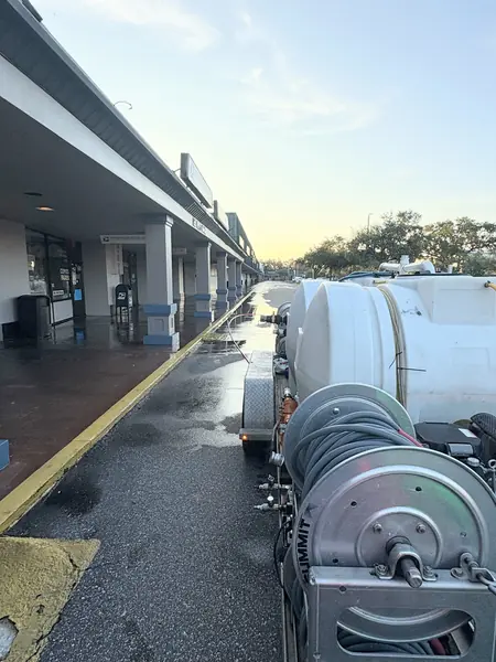 Hose reels and tank on a pressure washing trailer beside a wet strip mall sidewalk at dawn with a mail box in view