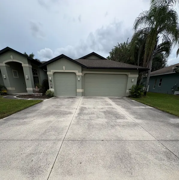 Stained gray concrete driveway in front of a three car garage on a stucco house under a cloudy sky