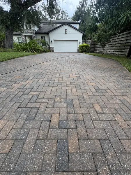 Herringbone brick paver driveway curving toward a two story home among trees