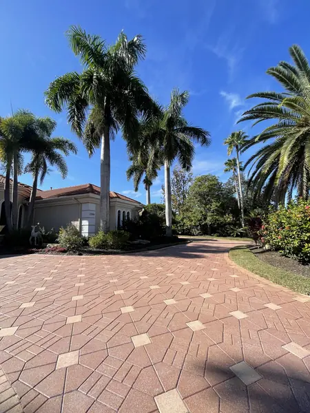 Clean red paver driveway with a diamond pattern curving toward a tile roof home under palm trees