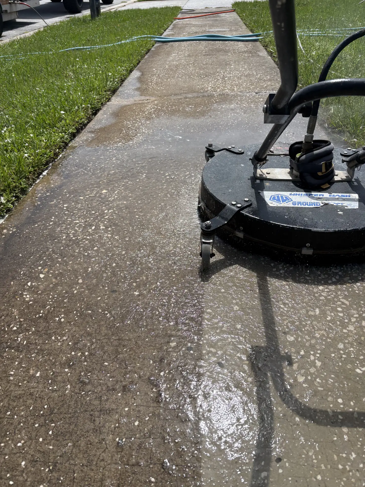 Gray rotary surface cleaner on a wet concrete driveway with a lighter cleaned path behind it