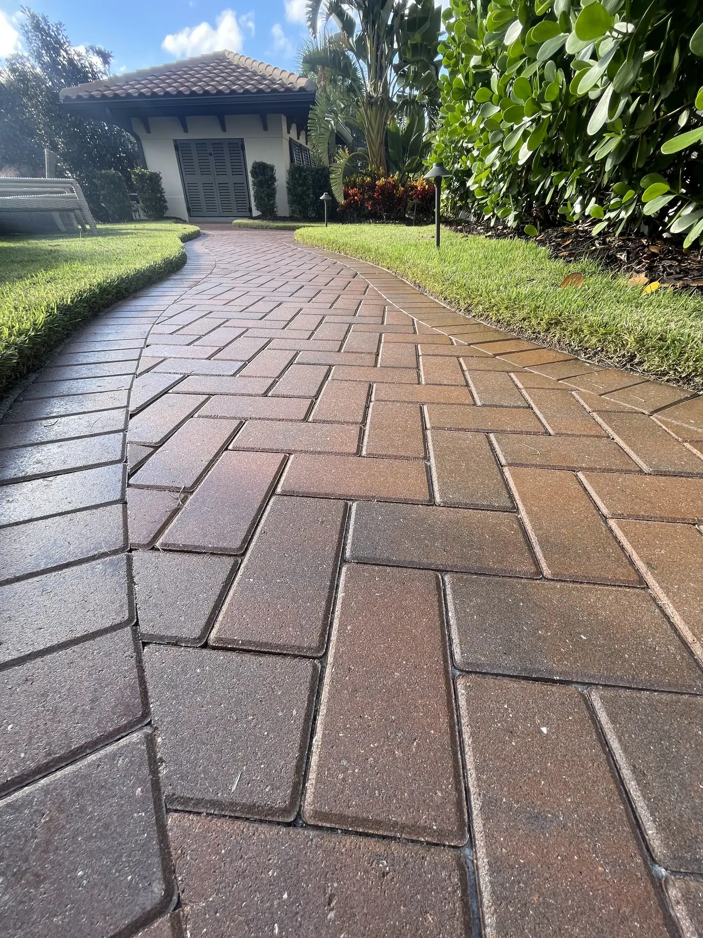 Brick paver walkway curving beside a lawn toward a house entrance