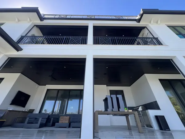 Upward view of a modern white building's balconies and dark ceilings under blue sky with a covered lounge below