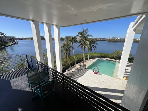 Waterfront terrace with a black railing, a pool and a speckled deck with a yellow surface cleaner at the right edge