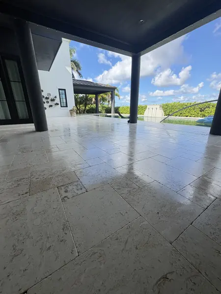 Low angle view of a glossy wet travertine patio under a dark covered porch, pool and cloudy sky beyond