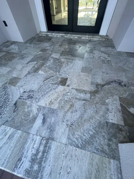 Looking down at a large grey veined stone tile floor beside tall glass doors