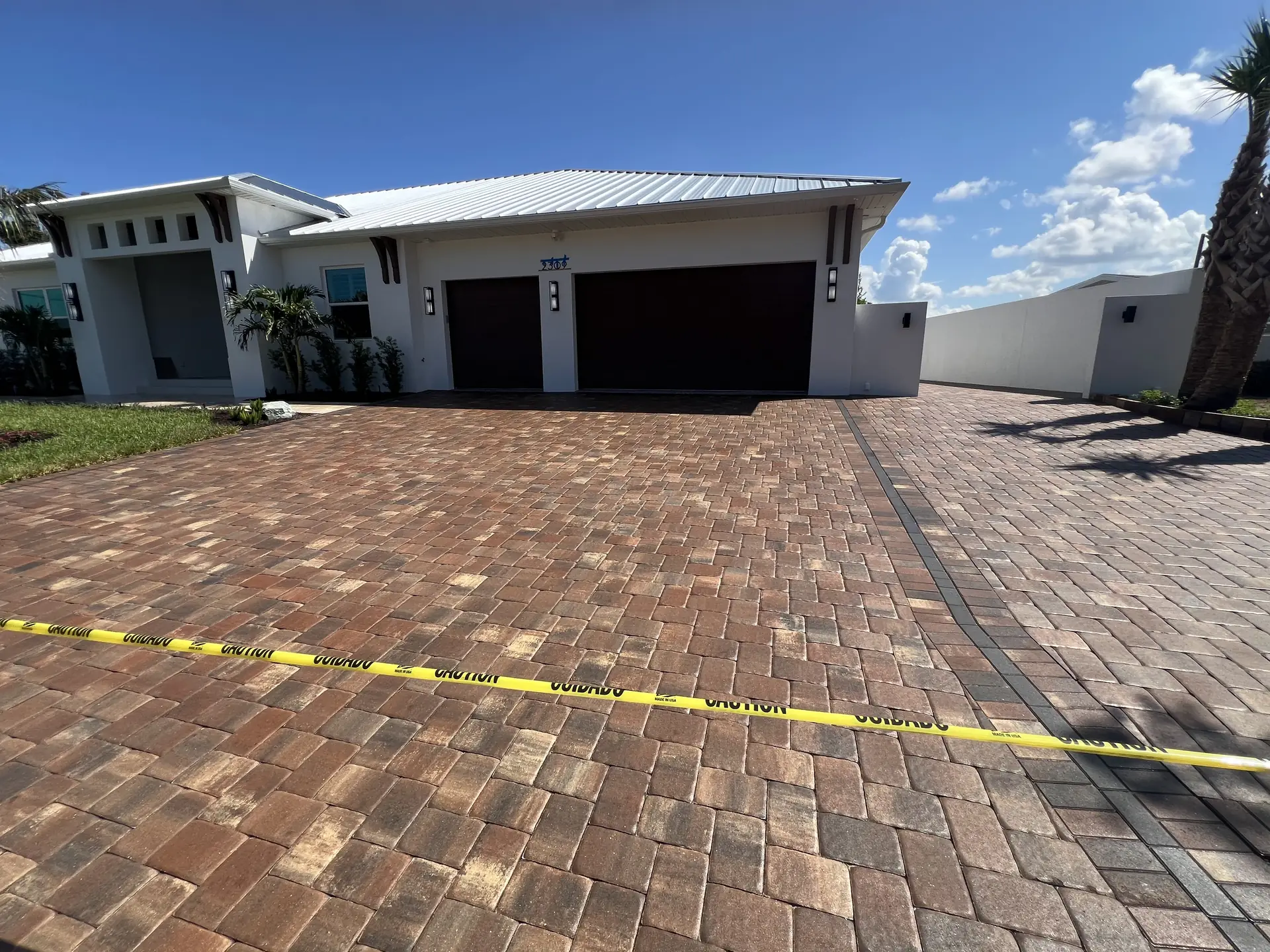 Brown and red brick paver driveway in front of a modern single story home with yellow caution tape across the foreground
