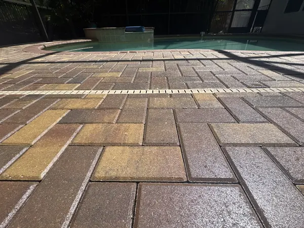 Low angle close view of multi-colored brick pavers with a drain channel running beside a screened pool