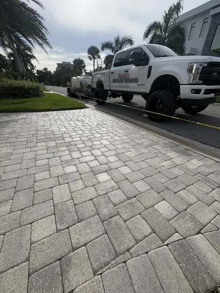 White service truck and wash trailer beside a freshly cleaned light gray paver driveway marked with caution tape