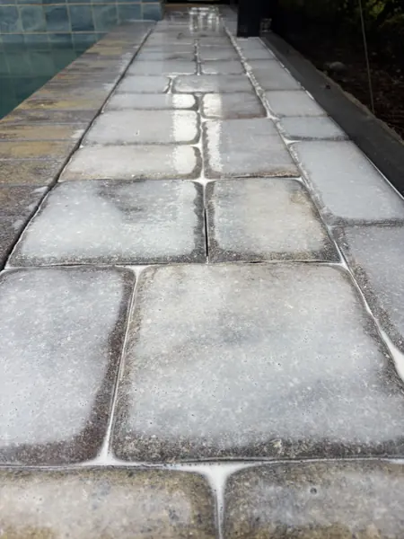 Low angle of large tumbled pavers beside pool coping with a milky white film on the surface and white lines in the joints