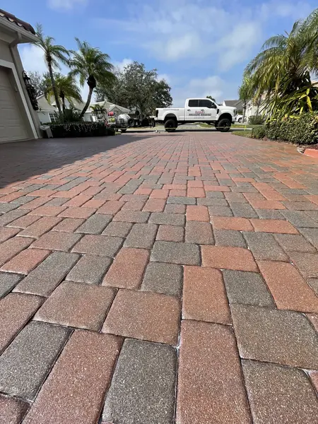 Red brick herringbone driveway on a residential street with the company truck and trailer in the distance