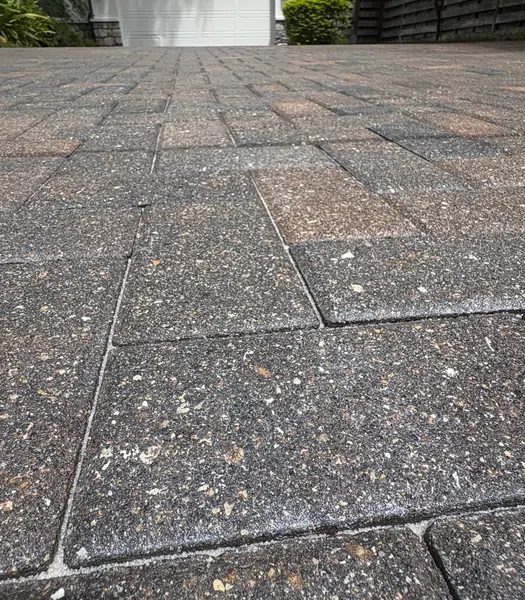 Low angle view of weathered gray-brown pavers with light joint sand and white powder, garage door in the distance