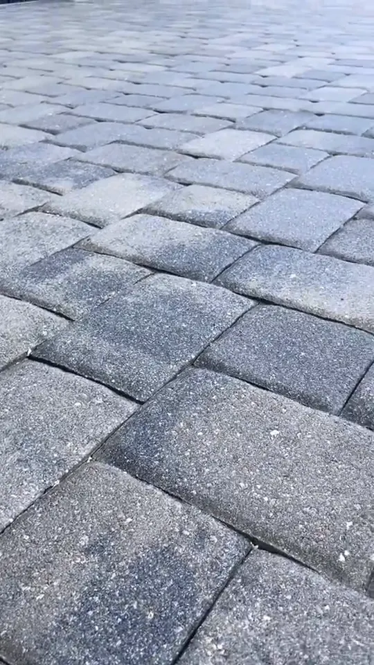 A surface cleaner and wand on a gray paver driveway, ending on the clean result.