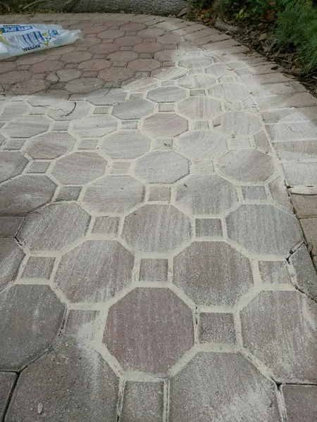 Octagon pattern paver walkway re-laid with pale joint sand dusted over the surface and a sand bag at the upper left