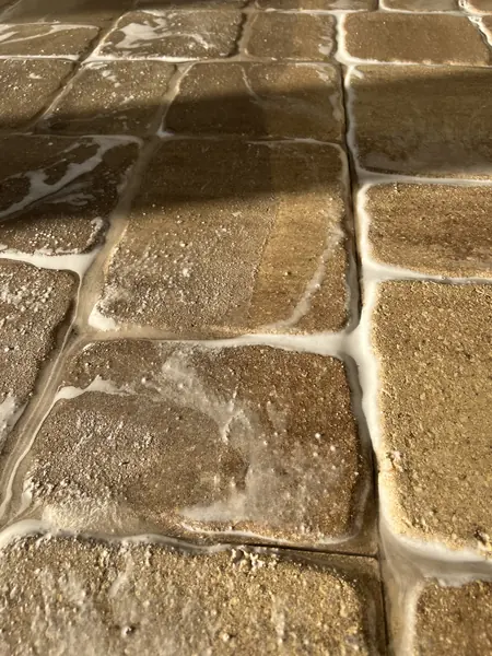 Close-up of tan tumbled stone-look pavers with white foam in the joints