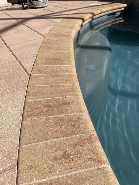 Close view of tan pool coping and deck pavers curving around the pool edge