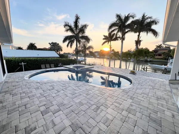 Brick paver pool deck at sunset with a kidney shaped pool, palms and a waterway behind