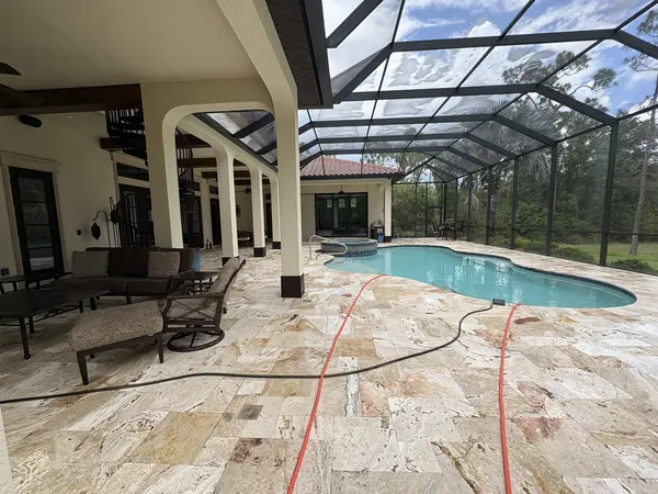 Pool enclosure with a cream travertine deck, orange and black hoses across the floor and soap residue on the screen roof